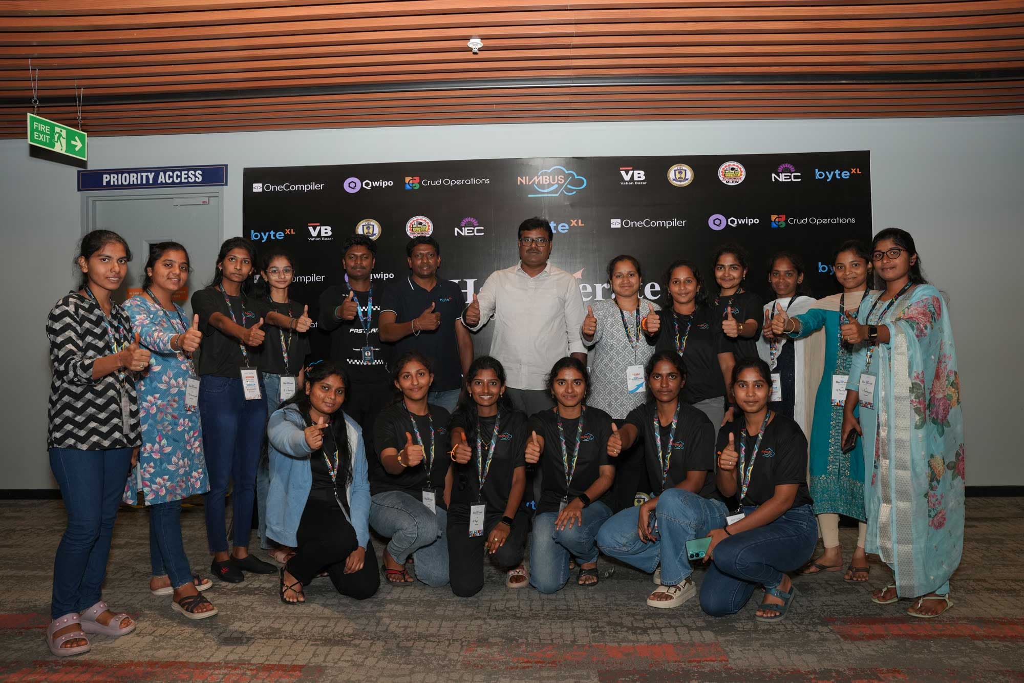 Participants giving a thumbs up in front of the HacXLerate backdrop